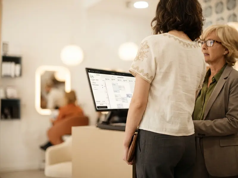 Two people at the front desk with the day’s book open on the monitor